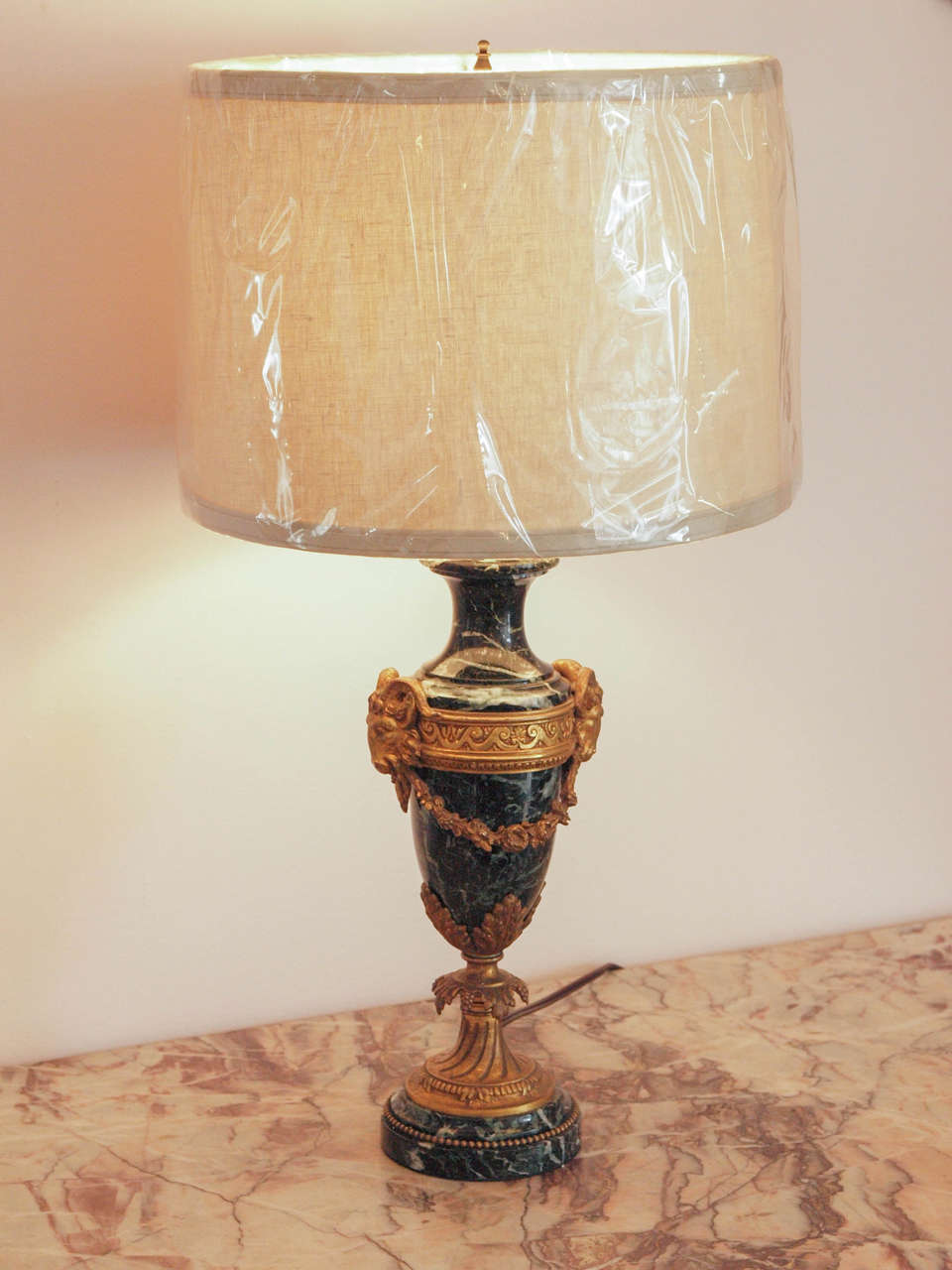 Stately Empire style urn shaped marble table lamp with neoclassical gilt bronze ornamentation including rams' heads mounted on a guilloche beaded band, floral festoons and acanthus leaves.  The lamp has been re-wired for USA.  Linen shade is