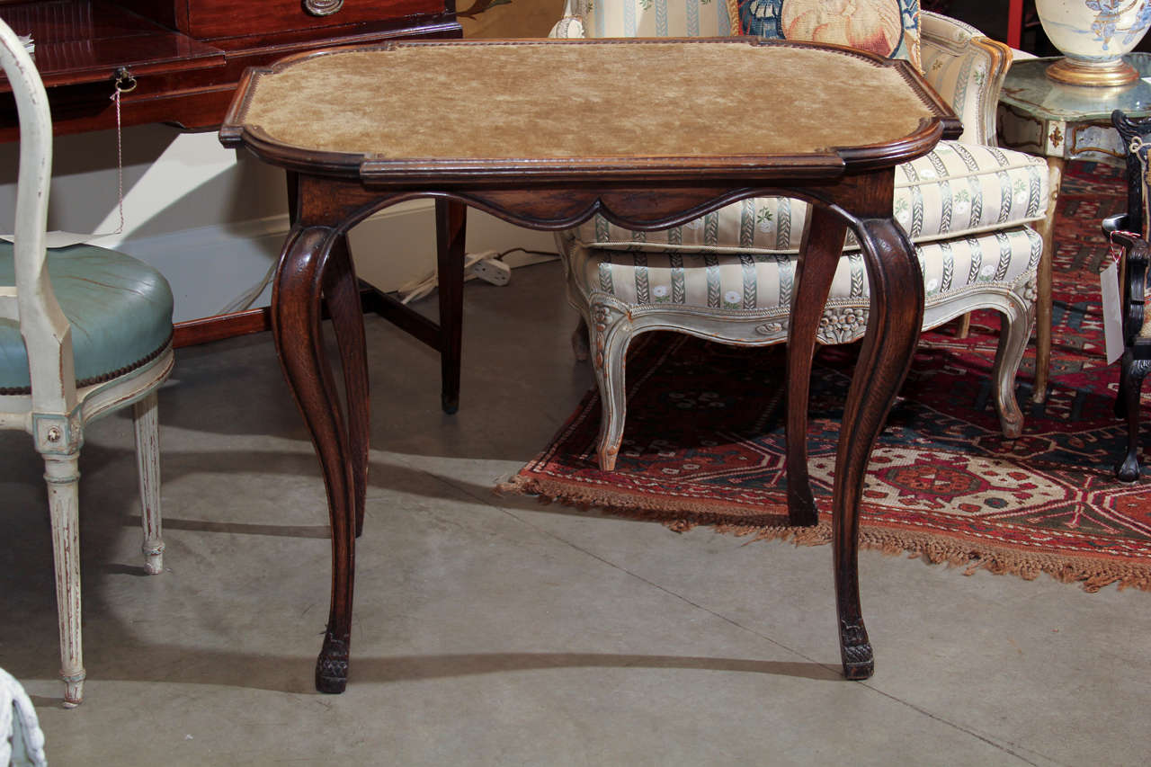 A late 19th or early 20th century Colonial Revival oak table with a shaped top inset with nail studded linen velvet.