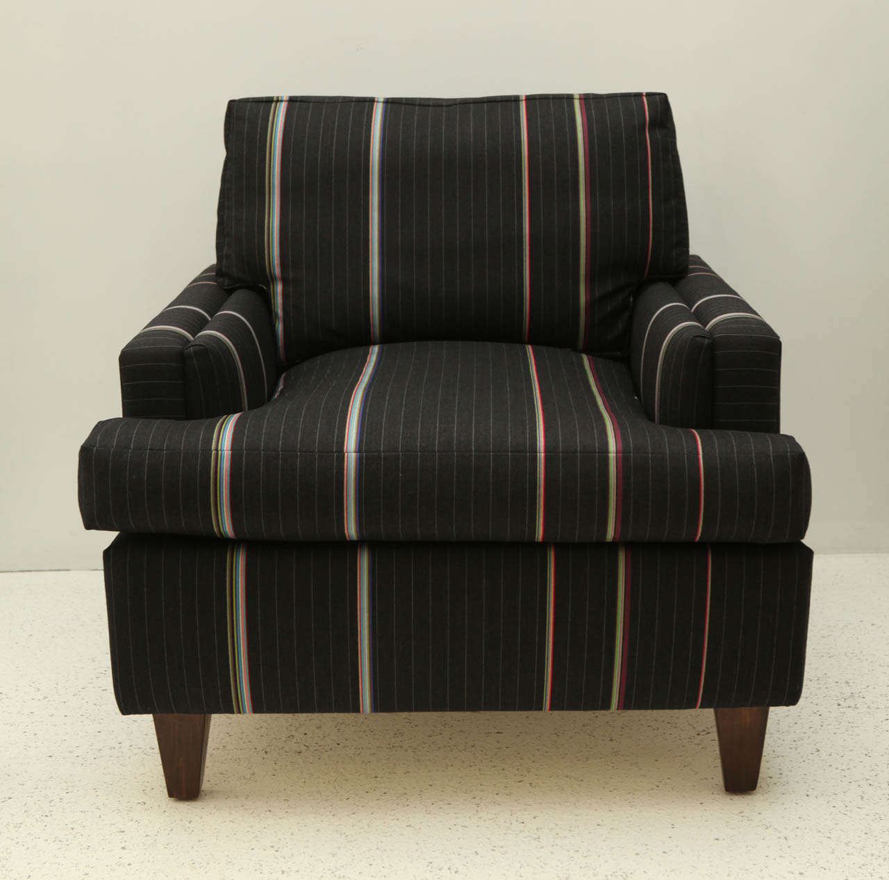 A handsome pair of club chairs, reminiscent of Haines classic Seniah, upholstered in a classic wool pinstripe fabric with a twist designed by Paul Smith for Maharam. The chairs have nice detailing and tapered walnut-stained legs.