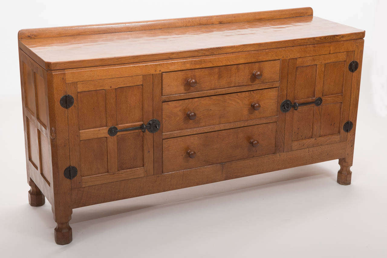 A Robert  “Mouseman” Thompson Oak Sideboard.
The adzed rectangular top with a short raised back.
Above central three graduating drawers with turned handles, flanked by a pair of four indented panel doors with iron hinges and latches.
On short