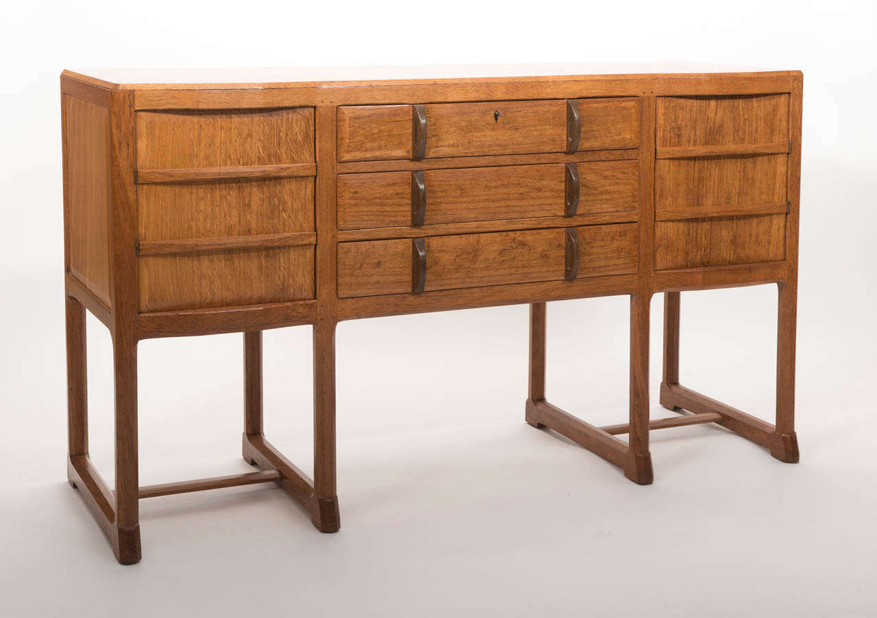 An early Oak Sideboard by Gordon Russell in the Cotswold school style.
Two cupboards and three drawers with bog Oak handles.
On eight sectional legs united by chamfered edge stretchers.
The interior cupboard doors with fine brass hinges.
Label