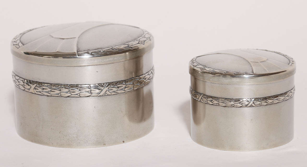 This pair of silver-plated boxes each has a lid with a geometric design and ears of wheat around the edge and wheat around the circumference.
Hallmarks: WMF/G with ostrich and beehive/ ALPACCA/ I/O in rectangle

Dimensions of larger box:
Height 2