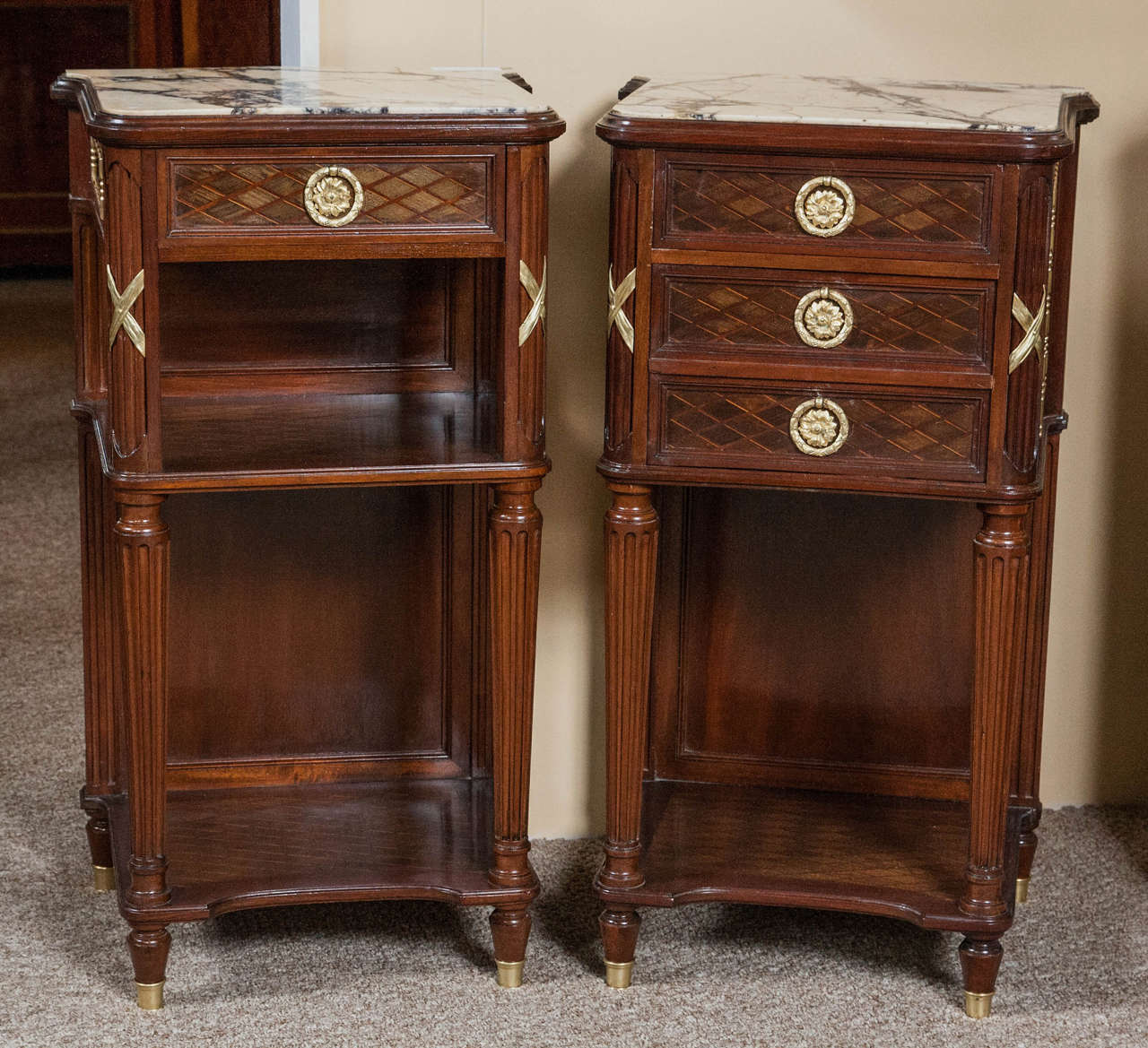 Pair of French Louis XVI Style stands or night tables. These wonderfully crafted crème tables have marble tops with grey and black veining and are possibly by Guillaume Grohé. One has three drawers with a basket weave design with brass pulls. The
