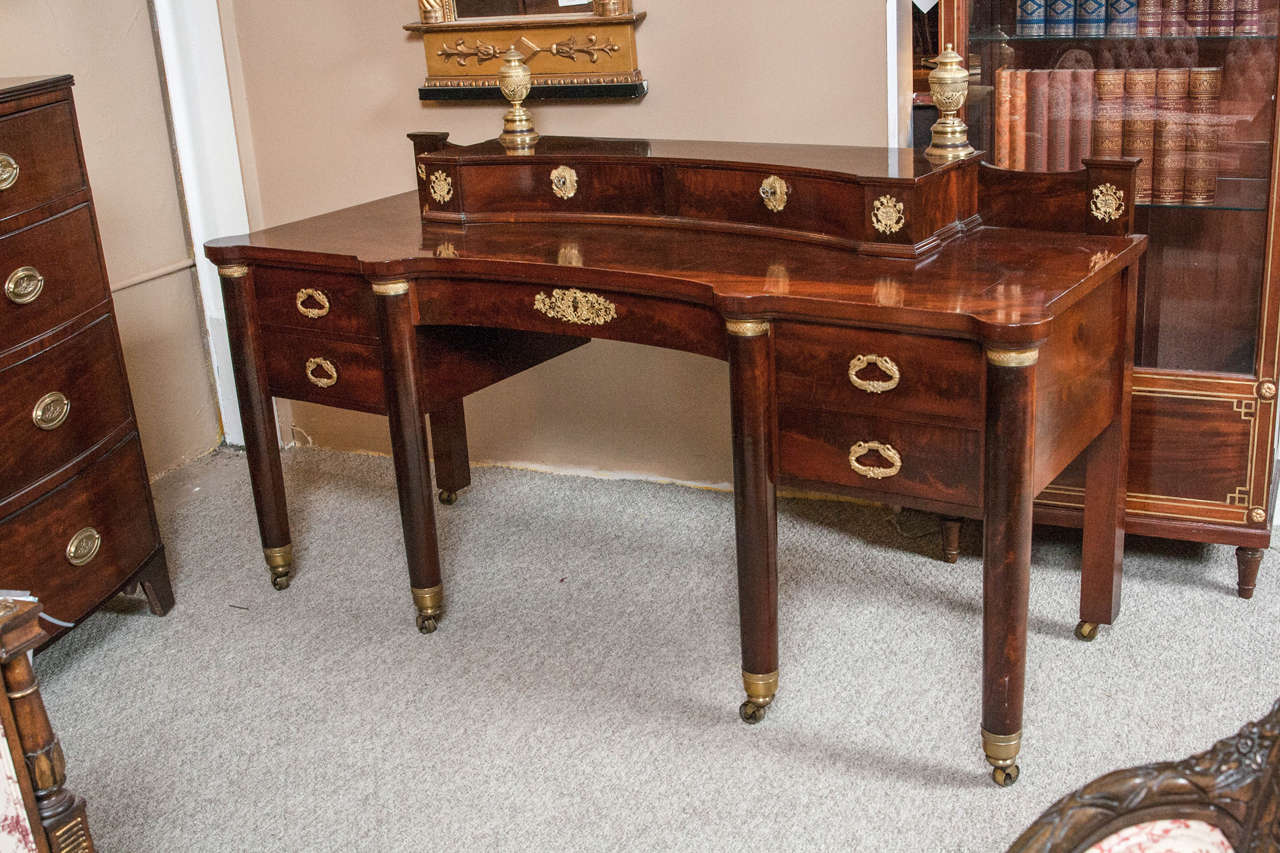 Mahogany Empire writing desk, circa 1860s. This fine flame mahogany desk has a center drawer flanked by a pair of side drawers and is supported by a group of bronze sabots on casters each supporting a cylindrical leg terminating in a bronze cap. The