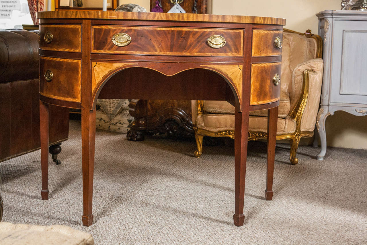 A baker satinwood and mahogany demilune server sideboard. Fine custom quality diminutive sideboard by the Baker Furniture company. Consisting of oak secondary's and fabulous satinwood flame and fan inlays. The satinwood inlaid and banded top