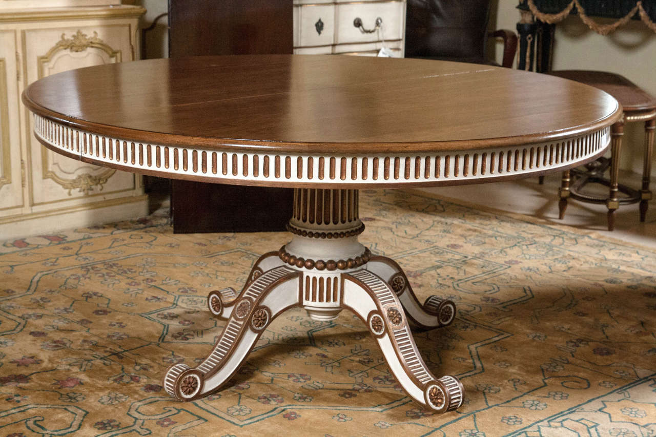This fine custom quality dining table is circular in form and extends to a large oval having three leaves each of 18' in width. The single pedestal base having quad legs all painted in a Swedish and gold paint decorative design. The solid mahogany