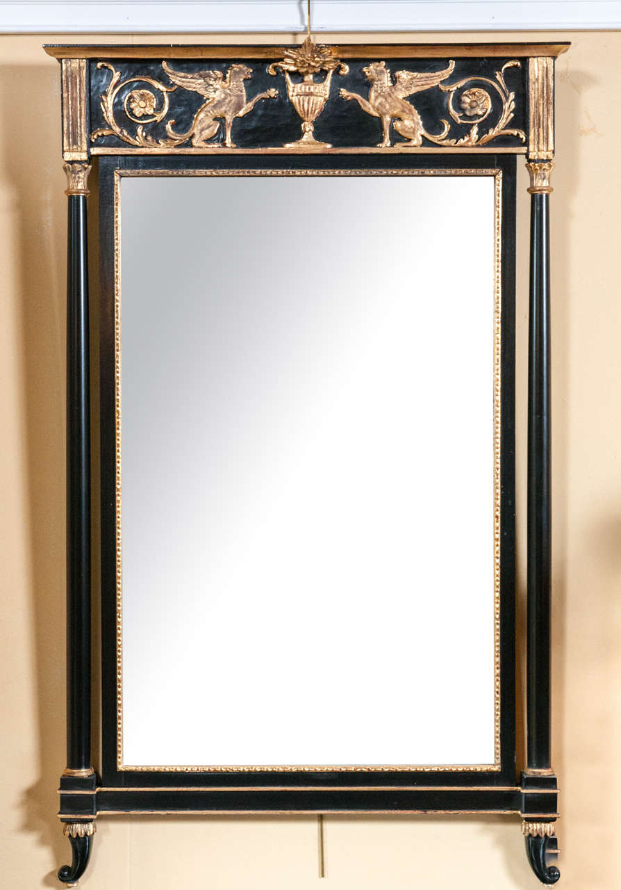 Russian neoclassical style pier glass mirror. This exquisite wall mirror in ebony and giltwood finish has a central mirror panel flanked by column form sides terminating in capitals supporting an upper apron having gilt winged lions pawing at a