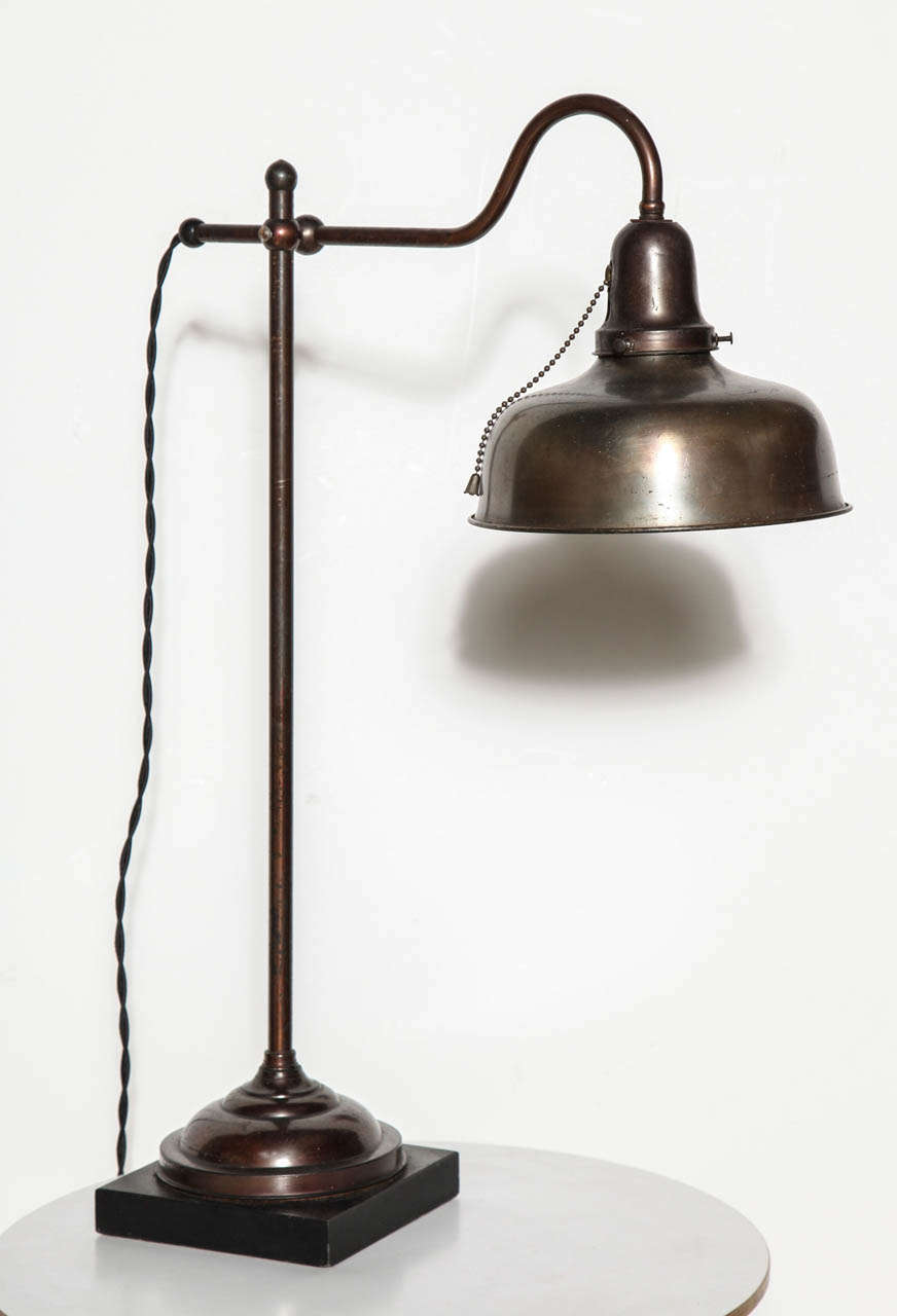 Circa 1900 Brass Student Reading Lamp on Black Slate base. Featuring an All Brass tubular stem, hook neck detail, 8 inch round hood bell shaped Shade, Off White enameled Shade interior and seated on a 6 inch square Black Slate base. Beautiful