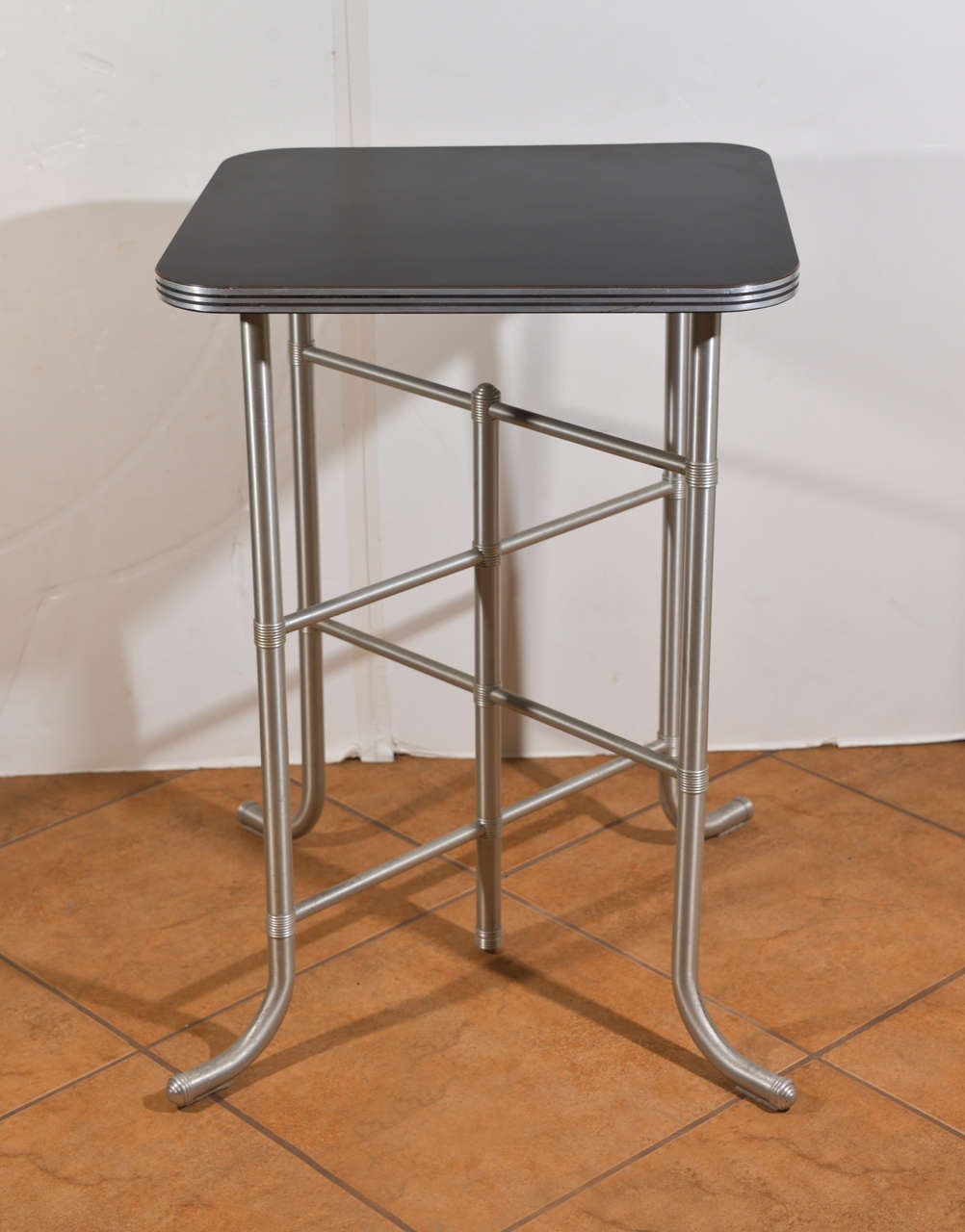 Anodic aluminum, enamel, rubber  and bakelite tall table.  One Park Avenue era.  Unrestored original condition.  
One of his better architectural criss-cross base designs.  
Visible stress cracks where feet curve out to floor, typical wear to