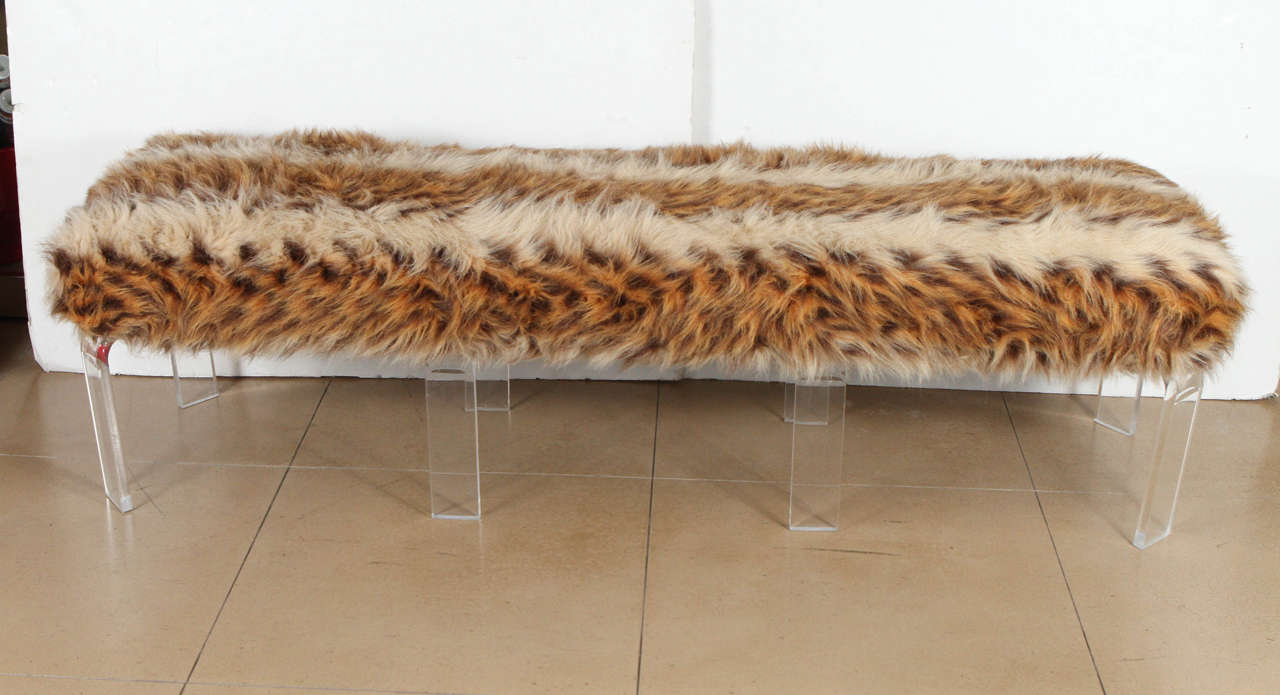 1970’s lucite bench upholstered in a faux fur hide with carmel, white, and brown striations affixed to eight clear lucite legs