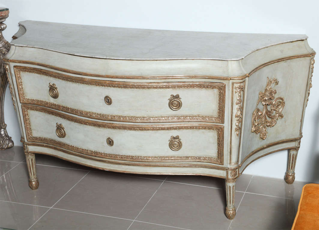 The inset Carrara marble top over a curved plain frieze with moulded edge in white gold, the two drawers with carved egg and dart moulding and original hardware and keyhole, the serpentine form sides with carved bellflowers and foliate motifs above