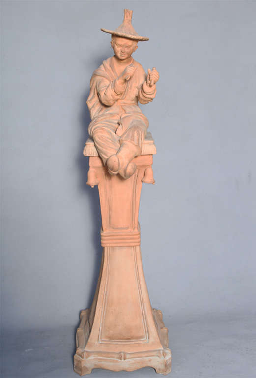 Cast figure of a Chinese man seated on a pillow, on tall base decorated by bells.