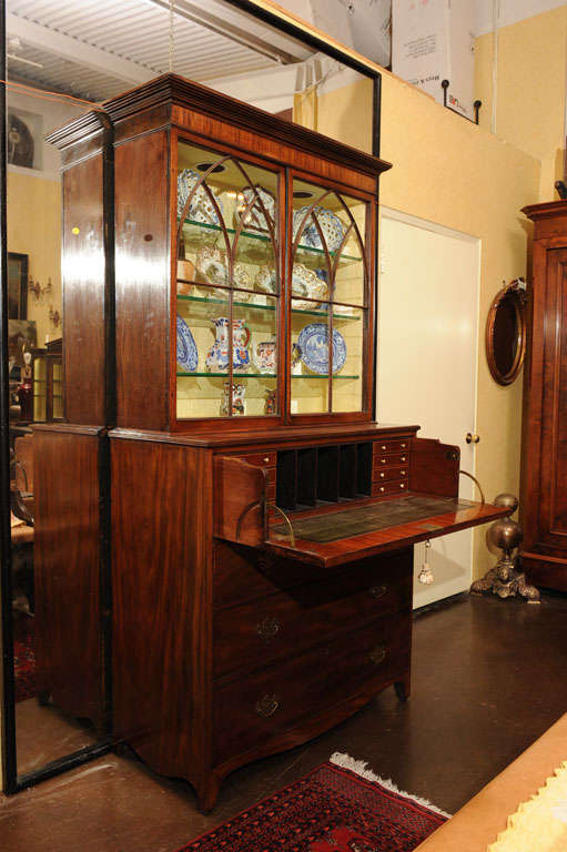 A GEORGE III MAHOGANY SECRETARY-BOOKCASE WITH GOTHIC STYLE ASTRAGAL-GLAZED DOORS BENEATH A REEDED CORNICE AND CROSS BANDED FREIZE ( THE ELECTRIFIED, GLASS- SHELVED INTERIOR INSERT REMOVABLE, WITH ORIGINAL 
SHELVES RETAINED), THE LOWER SECTION WITH
