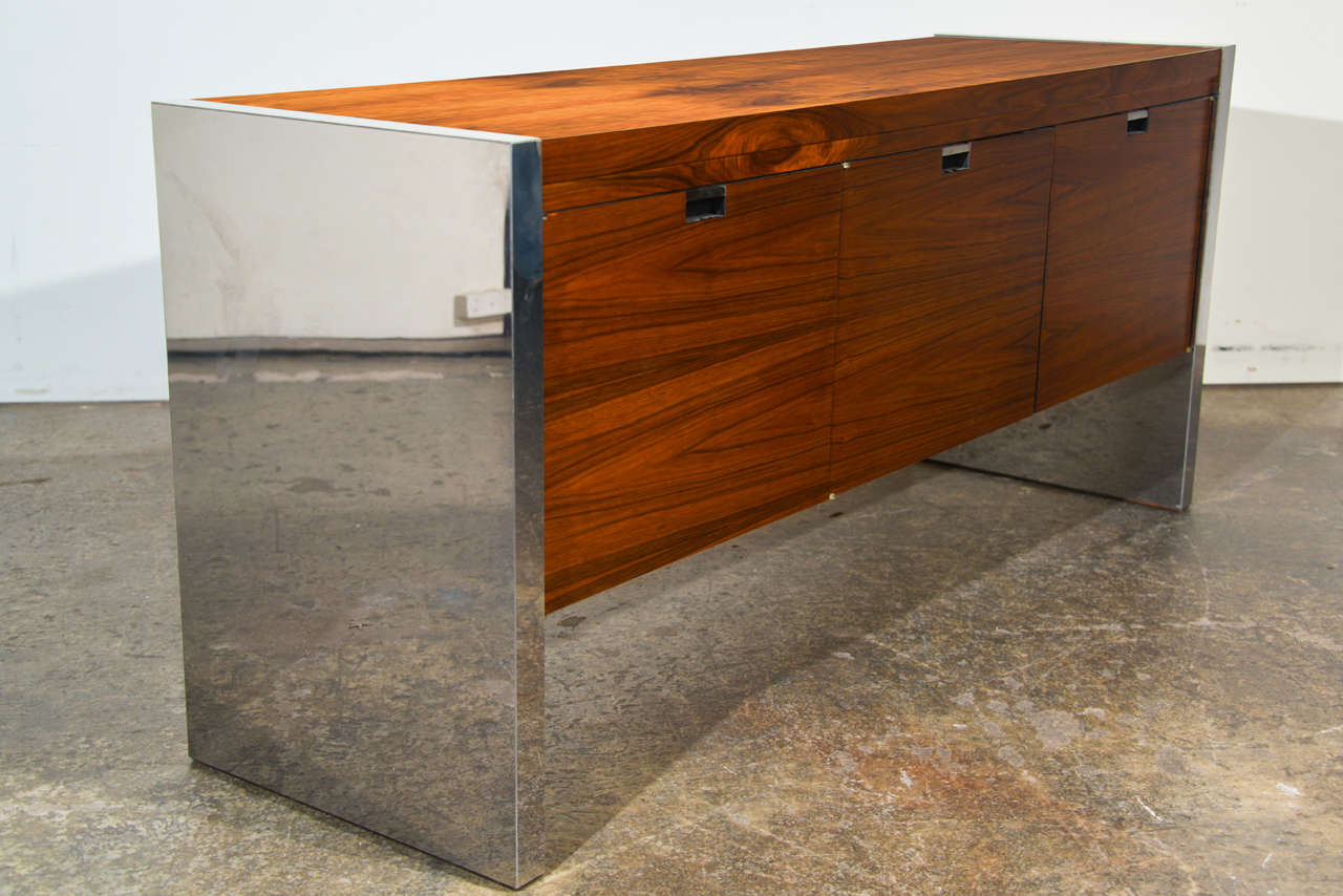 A mid century modern executive credenza designed by Roger Sprunger for Dunbar. The credenza is made of Rosewood and has chrome panels on both ends. The piece also has three door fronts that open to storage. We have a matching executive desk