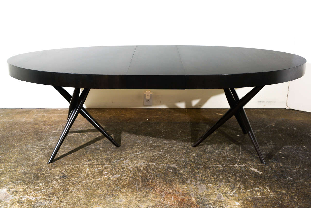 An oval walnut dining table with tripod bases by T.H. Robsjohn Gibbings for Widdicomb.
