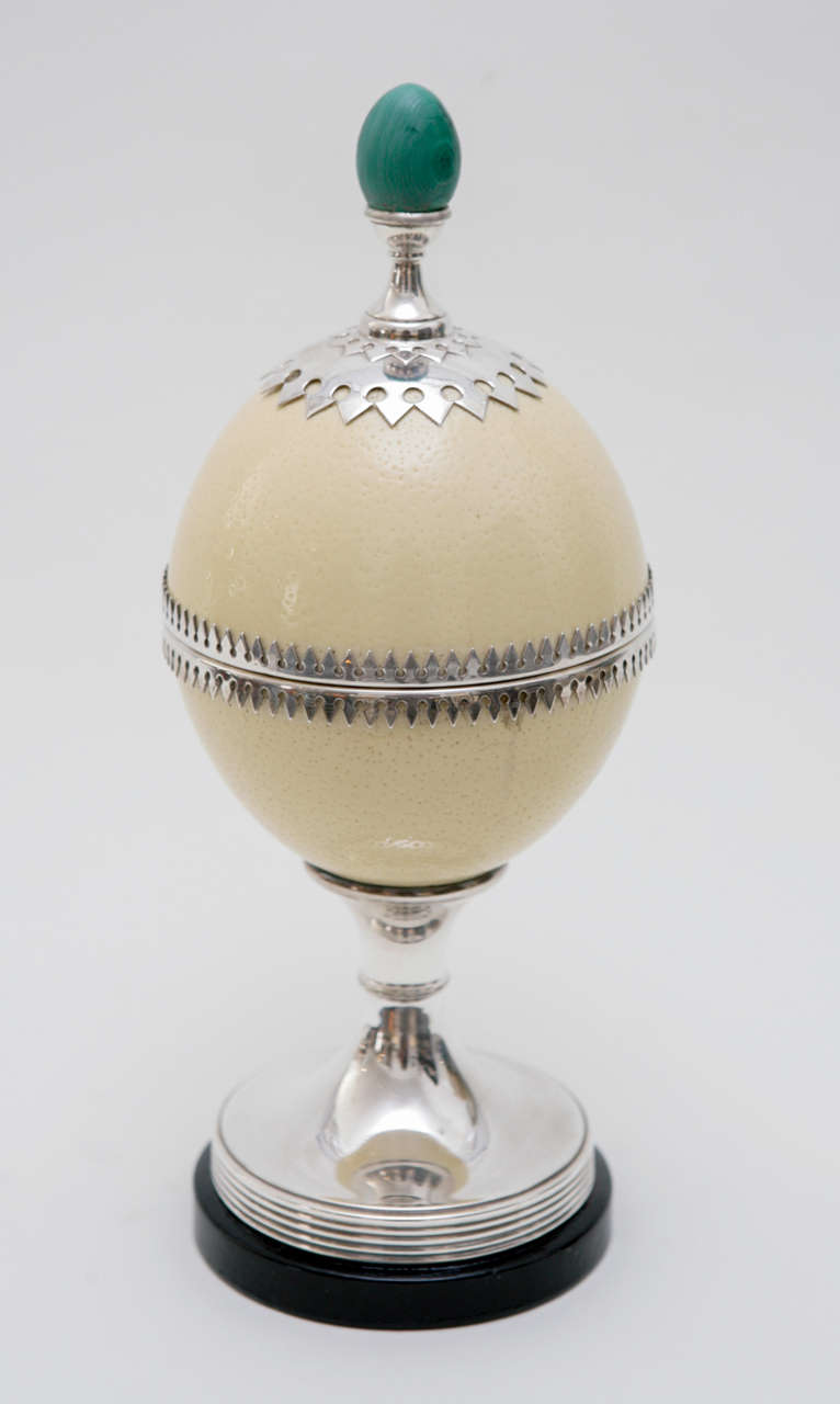 An unique footed ostrich egg box work that, though unsigned, is classic Redmile. The ostrich egg is accented with silver plate trim work, topped with an egg-shaped malachite finial and set atop a black lacquered wood base.