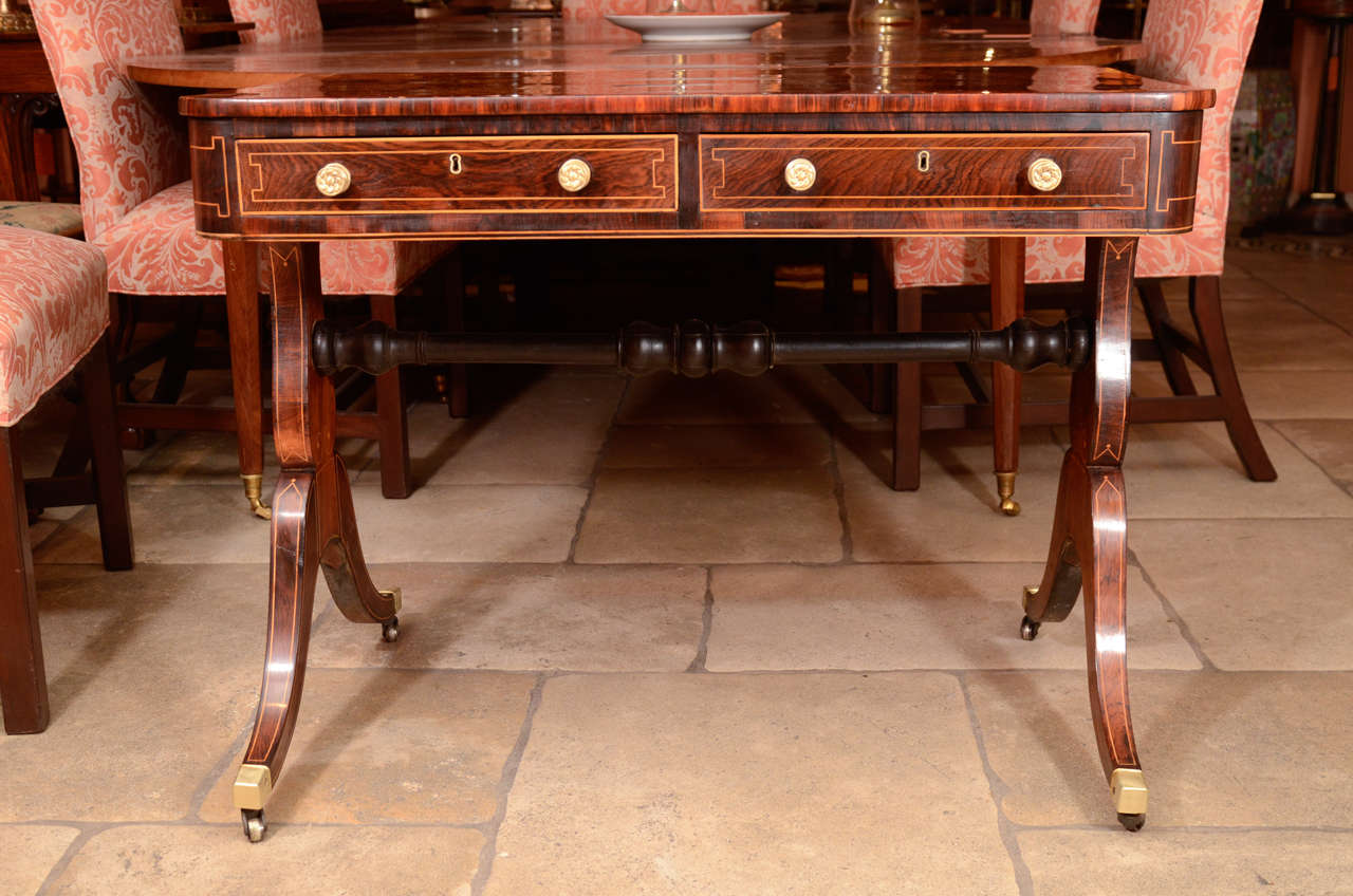 A fine and Regency rosewood crossbanded and satinwood line inlaid two-drawer writing table with trestle ends and brass castors.
