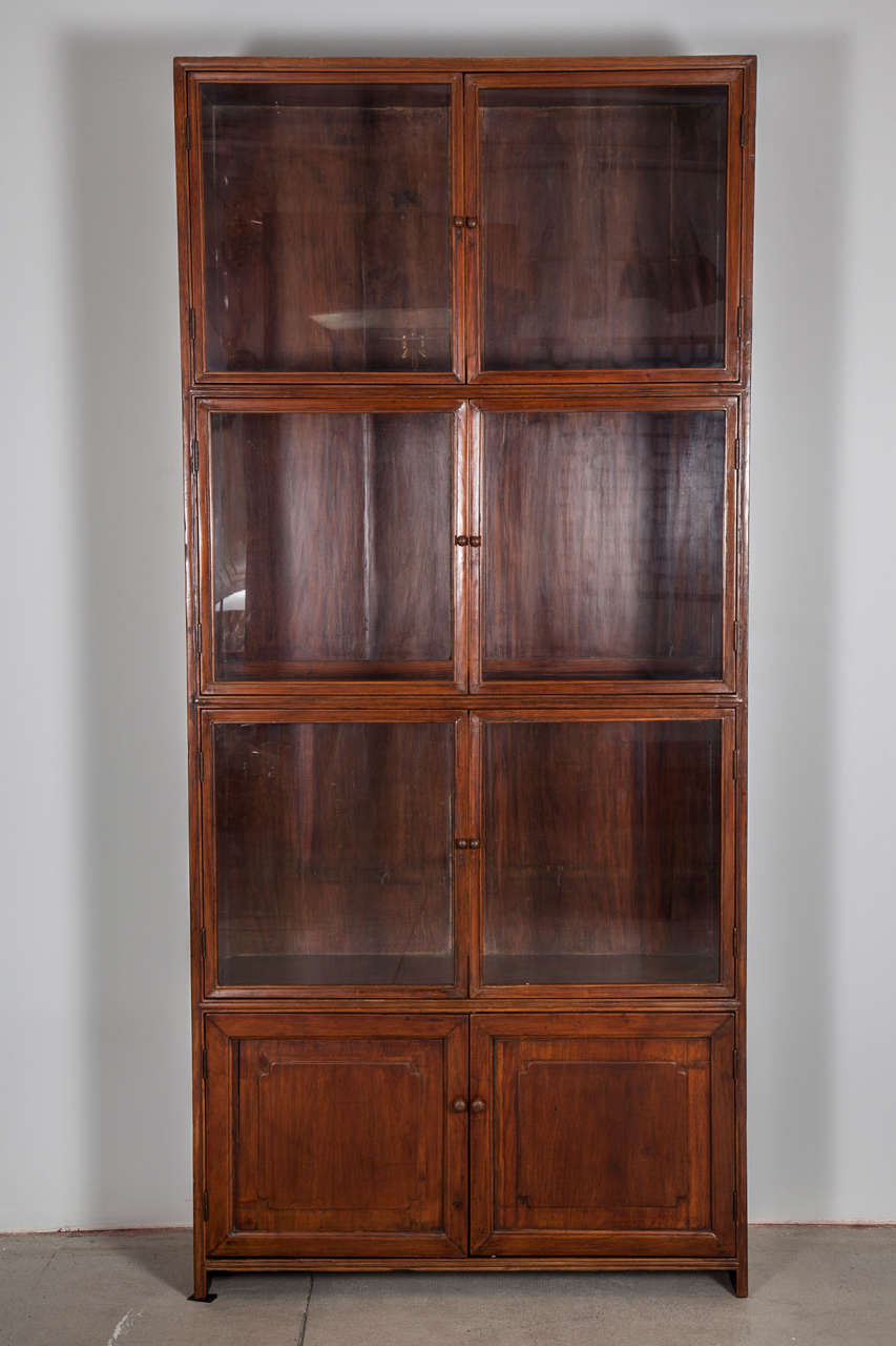 A Spanish Colonial narra wood bookcase cabinet, Circa 1900, in one piece, with three sets of glass panel doors above a set of lower panel cupboard door raised on square feet. 

A very practical cabinet that traverses both traditional and modernist