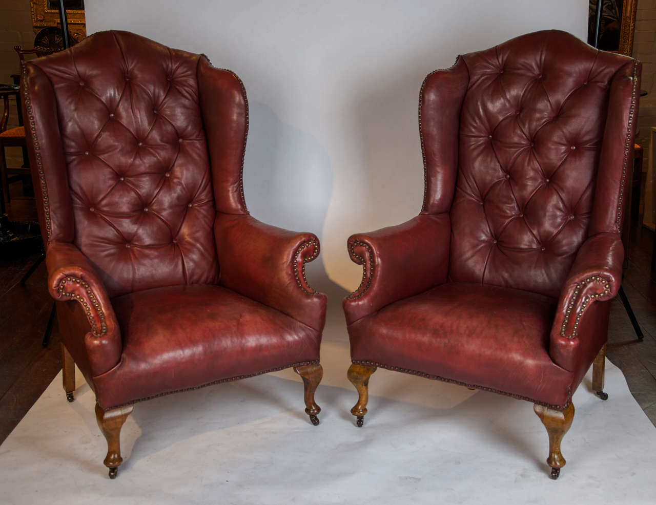 A good pair of early 20th century wing back chairs with original read leather and buttoned backs. Standing on beech cabriole legs to the front and splay to the back, terminating in ceramic castors.
