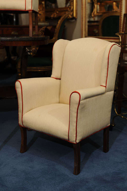 Each petite rectangular back flanked by two side wings above padded underscrolled arms and a square seat raised on straight legs; newly upholstered in cream with deep garnet piping.