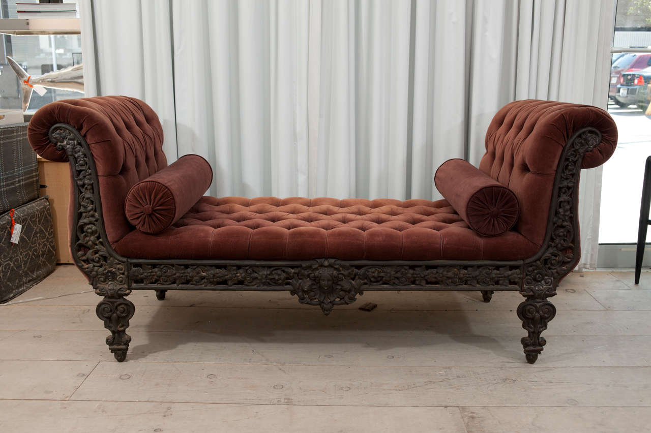 Elegant vintage French daybed upholstered in a soft, velvet fabric accented with deep tufting. The entire frame is solid iron with intricate detailing throughout.