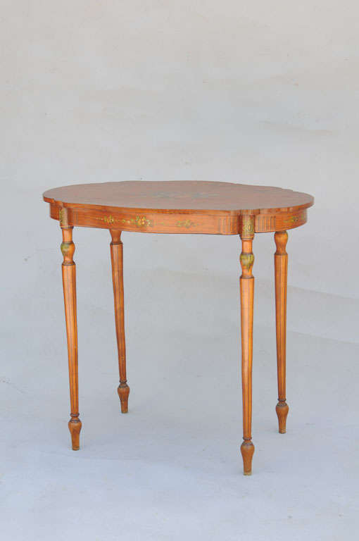 Oval table, of satinwood, having freeform shape top with exquisite handpainted floral details, apron with fluting and additional handpainting, raised on round tapering fluted legs with toupie feet.