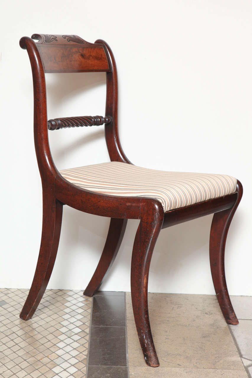 A set of 8 Regency mahogany klismos dining chairs, with incised scrolling crests over figured and brass outlined paneled crestrails, spiral carved and turned  back splat, drop-in seat and incurved front and back legs.