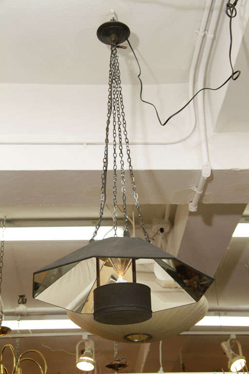A mirrored light fixture with a patinated metal center piece holding a socket. Up light reflects beautifully off a mirrored pyramid form in the middle as well as the larger, angled mirror tiles around.