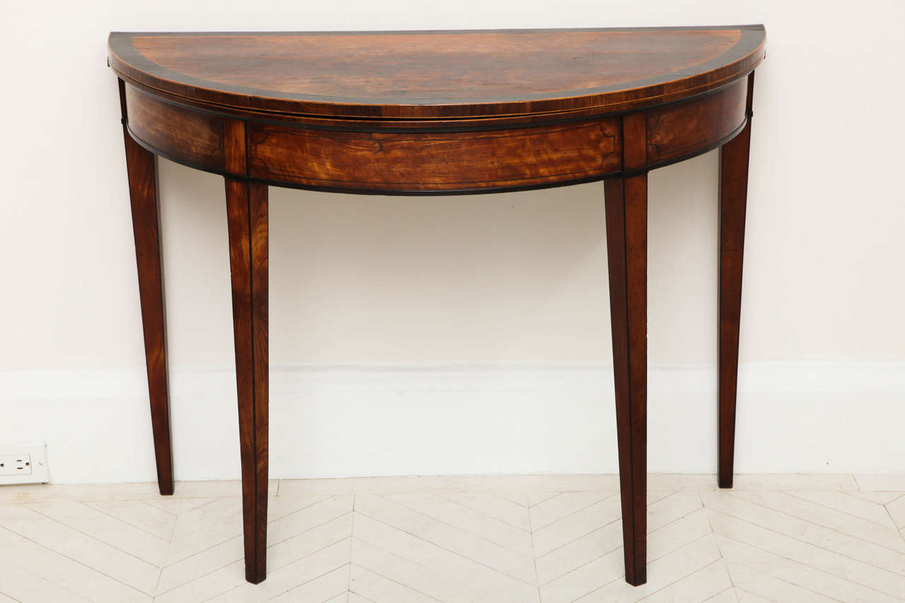 A George III satinwood and ebony inlaid demilune console opening to a round games or center table.