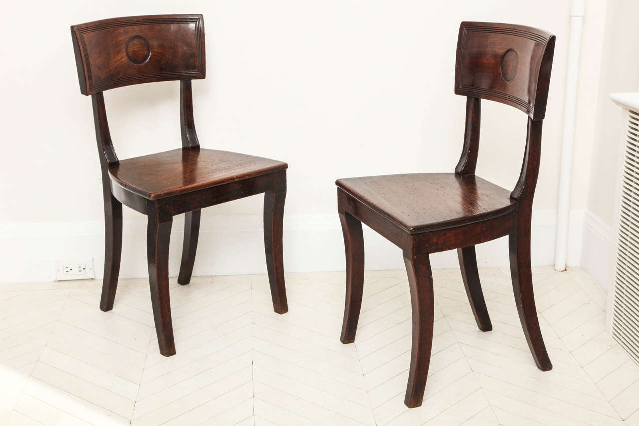 A pair of English Regency hall chairs with solid tablet backs geometrically decorated with incised stringing and central circles.