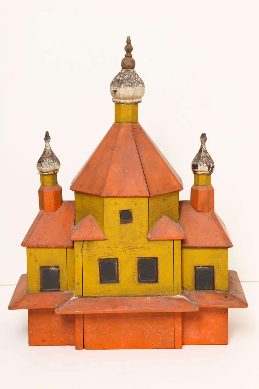 A fanciful painted wood birdhouse with glass windows and three turreted onion-dome spires with crackled original paint