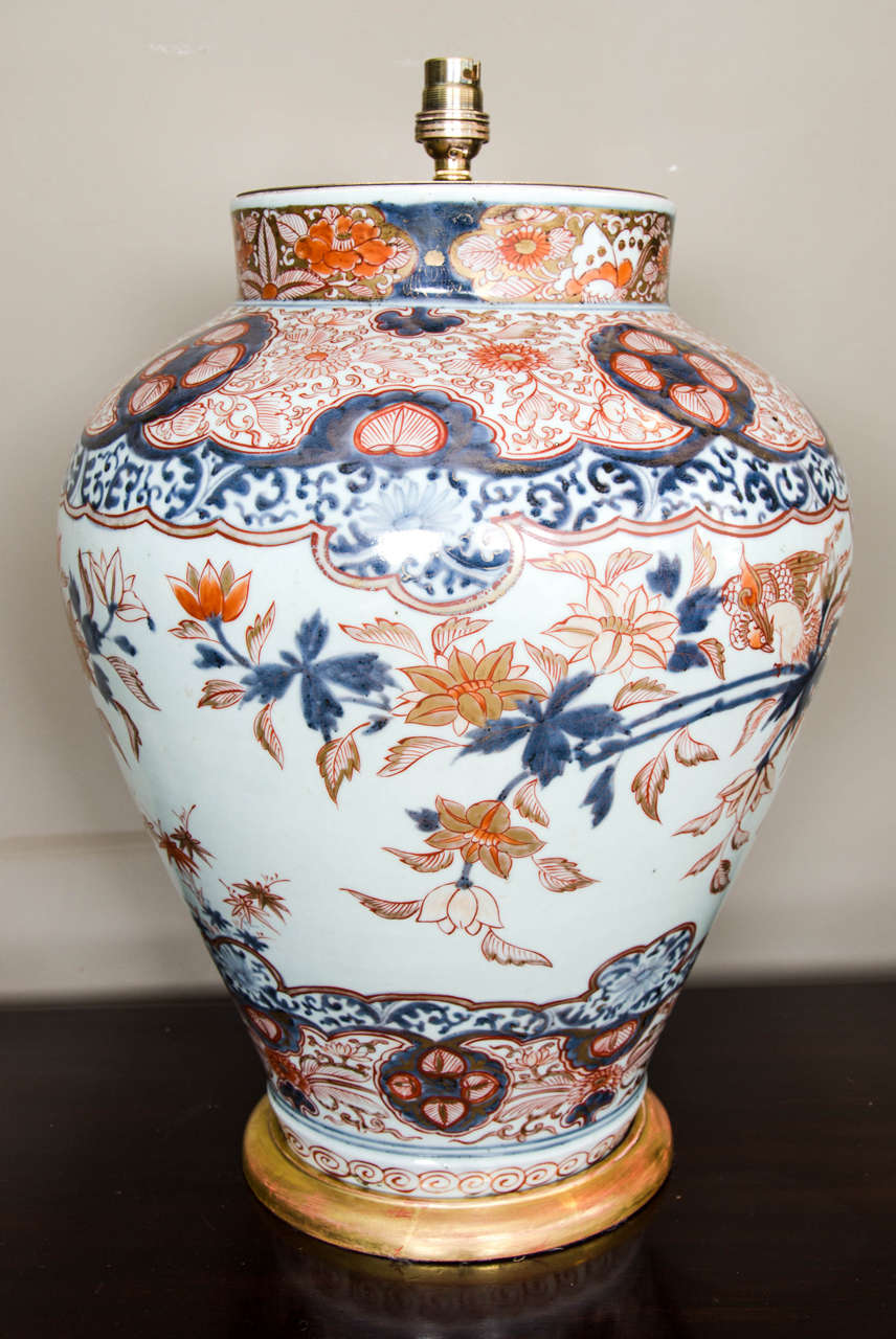 A large early 18th century lamped porcelain Japanese Imari baluster vase on a hand carved and water gilt wooden base. The vase has been fitted with antiqued brass plates and light fitting. The vase is decorated in beautiful muted colours, the
