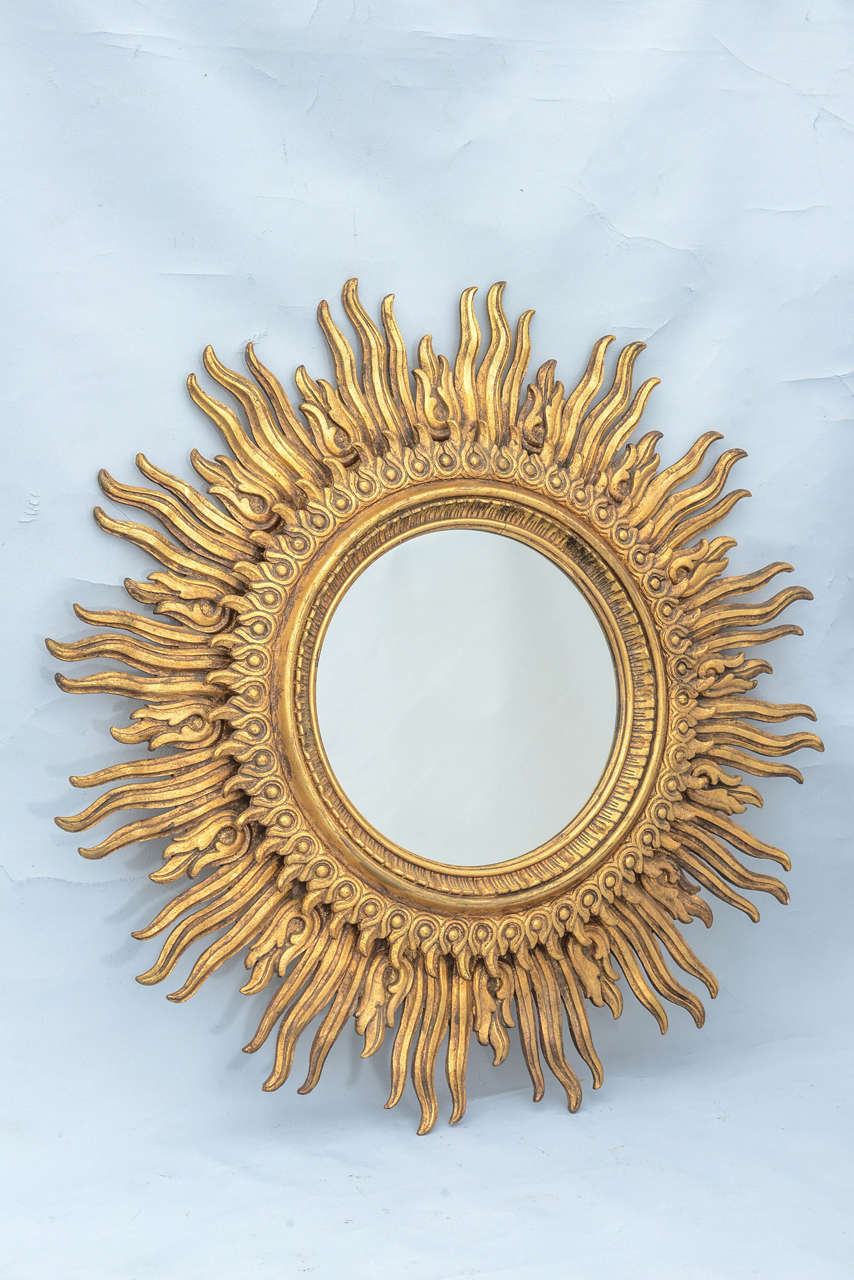 Sunburst mirror, in grand scale, of carved giltwood, having a round mirror with a border of combing, and two tiers of sunrays.