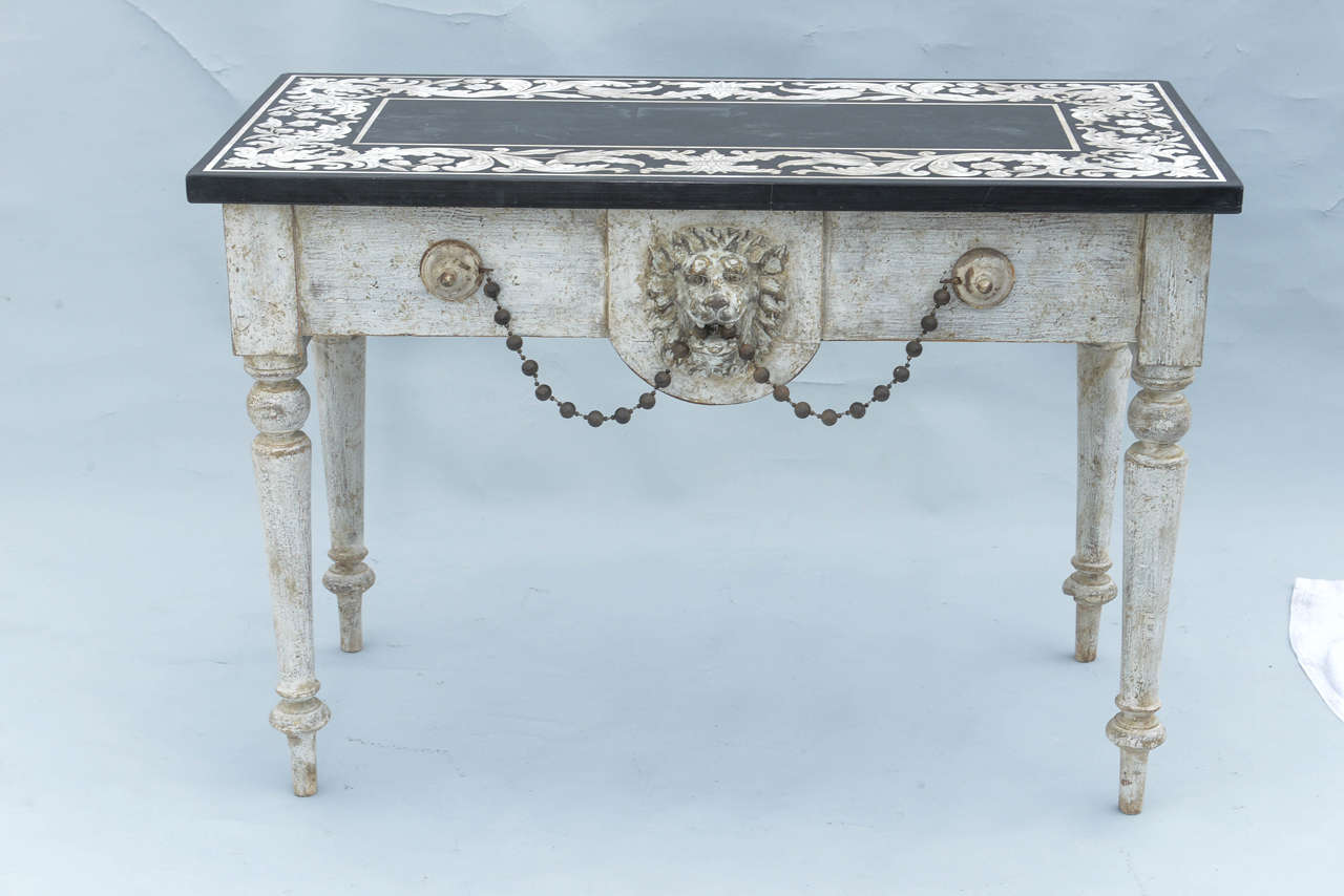 Console of antique elements, having a rectangular top of slate inlaid with marble in foliate design, on painted table base, its apron centered with lion's mask applique, flanked by discoidal accents joined with beaded festooning, raised on