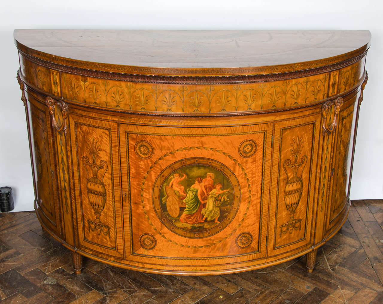 A fine quality 19th century satinwood Sheraton Revival demilune side cabinet, with inlaid and painted classical decoration. Having a single central door opening to reveal a shelf. Raised on square tapering legs.