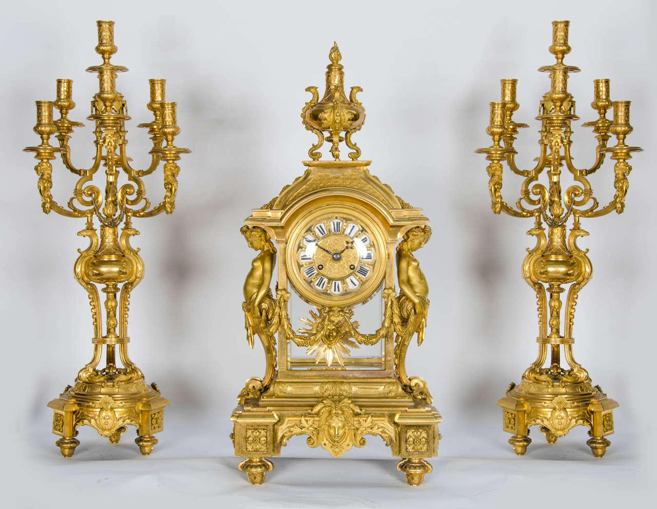 A large and impressive, very good quality French gilded ormolu clock garniture. The clock supported by a pair of Caryatids, decorated with swags and classical motifs, four bevelled glass panels and a sunburst pendulum.
The candelabra each having