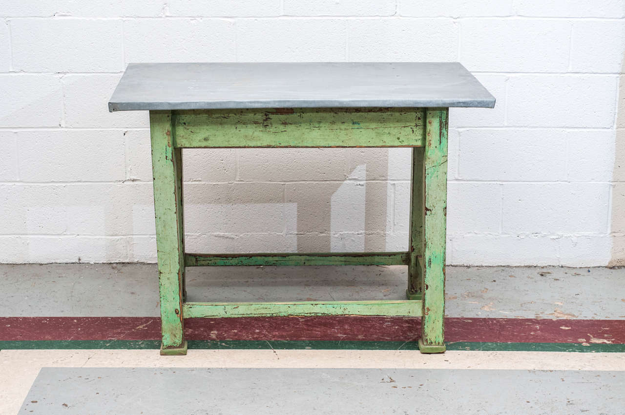 A beautiful zinc-topped work table on a square-legged stretcher base.  Shades of green paint are worn through to original burgundy and then to exposed wood for a delightfully rustic finish.