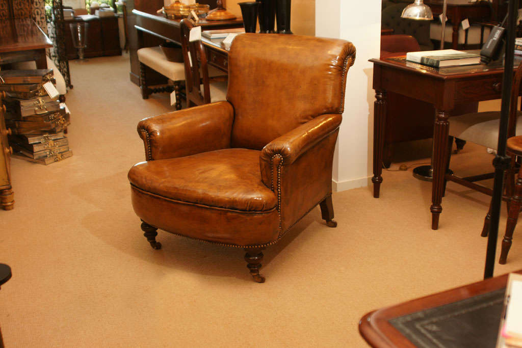 A wonderful rolled arm and rolled back 19th Century library club chair upholstered in a glossy tobacco leather detailed with brass nail heads sitting on mahogany bun feet with brass casters.  Very comfortable, very special.