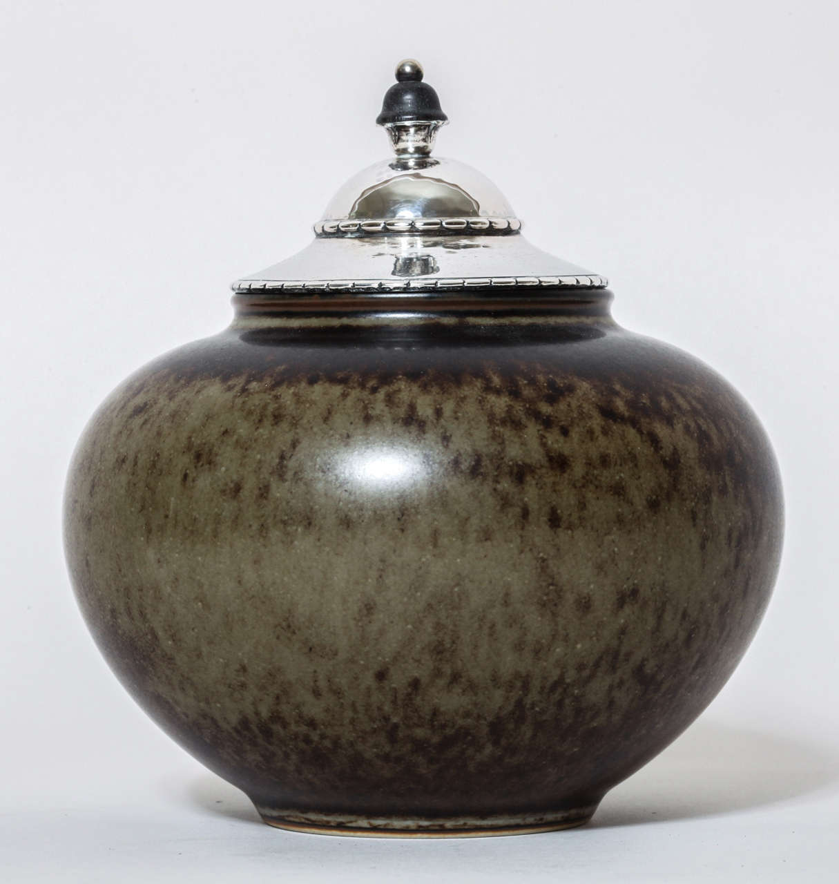 This covered pot has an mottled ochre brown glaze with a beautiful silver top with ebony finial.
Pot is signed with printed factory marks HHH & 20517.
Lid with Denmark sterling silver stamp for 1920/ Assay Master C. F. Heise monogram/ D and A with