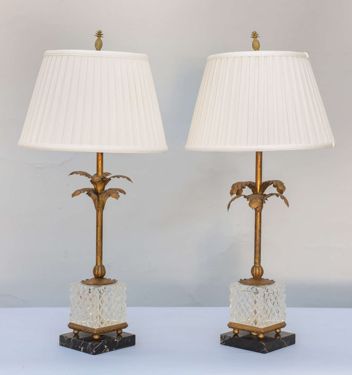 Pair of lamps, each a palm tree of gilded iron, in a cube shaped "planter" of diamond pattern glass on ball feet, set upon a square plinth of black marble.   Shown with shades (not included).

Stock ID: D6900