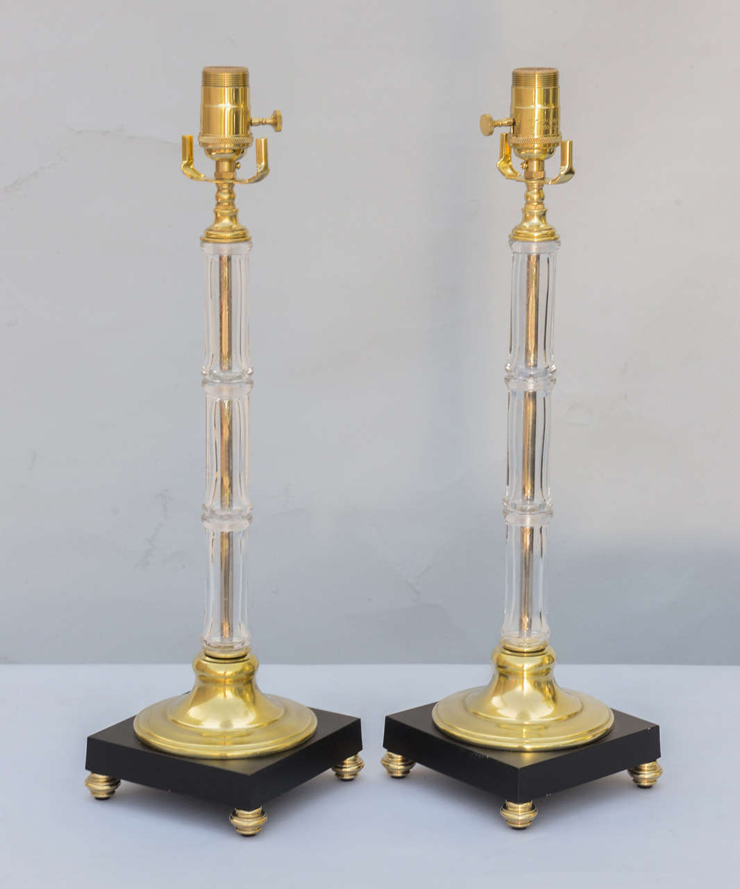 Pair of lamps, by Warren Kessler, each a glass "bamboo" stalk on round brass base and square black plinth raised on brass bun feet.