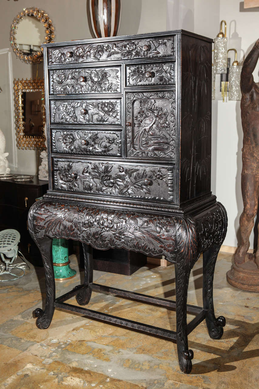 Elaborately carved ebonized hardwood tall chest on stand, Japanese Meiji period, in the Aesthetic style. Middle drawer on lower section.  Imported by Hampton & Sons LTD approximately 1900, long-time 19th-20thc English furniture maker, retailer and