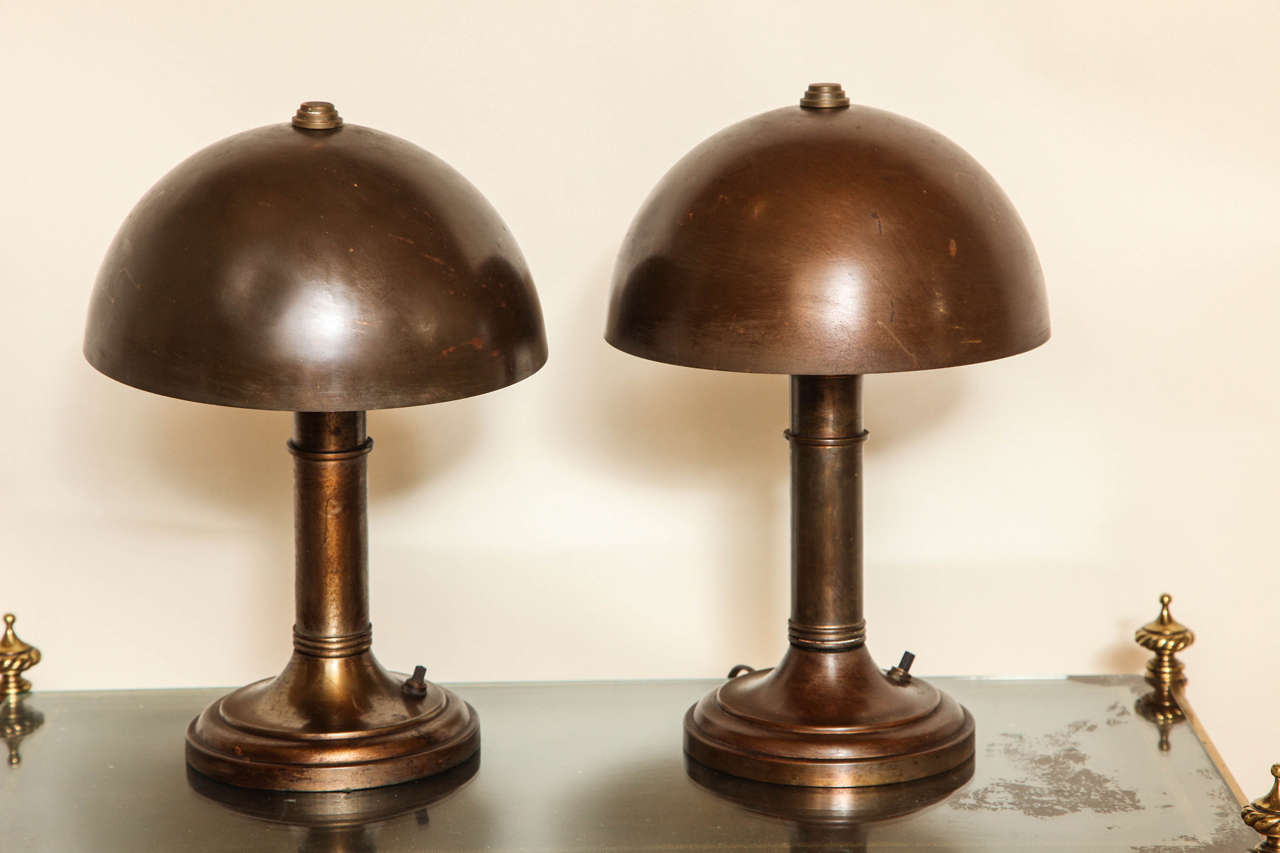 A pair of American patinated metal table lamps with round bases and dome shaped shades concealing one Edison socket.