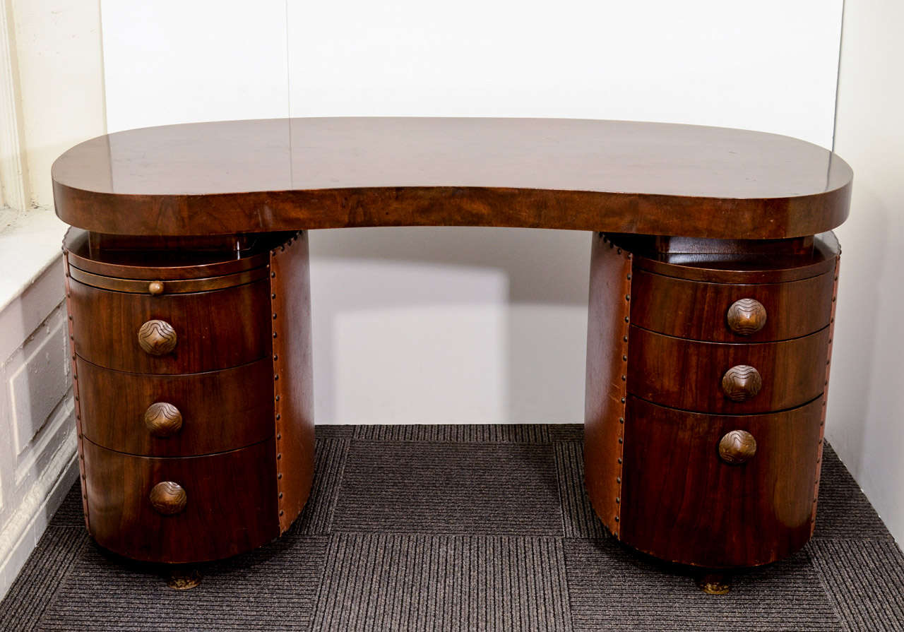 A vintage Gilbert Rohde Paldao double pedestal desk produced by Herman Miller. Biomorphic top with six drawers and pull-out writing surface. Cone pulls with Art Deco form and design. Camel leatherette fabric trim with patinated brass tacking. It is