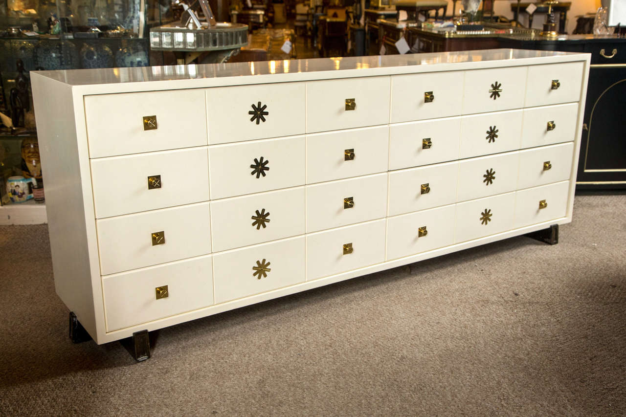 A mid-20th century modern white lacquered double chest designed by Tommi Parzinger. The rectangular case fitted with eight long side by side drawers mounted with brass pulls and decorative center panel mounts. The whole resting on a ebonized twin