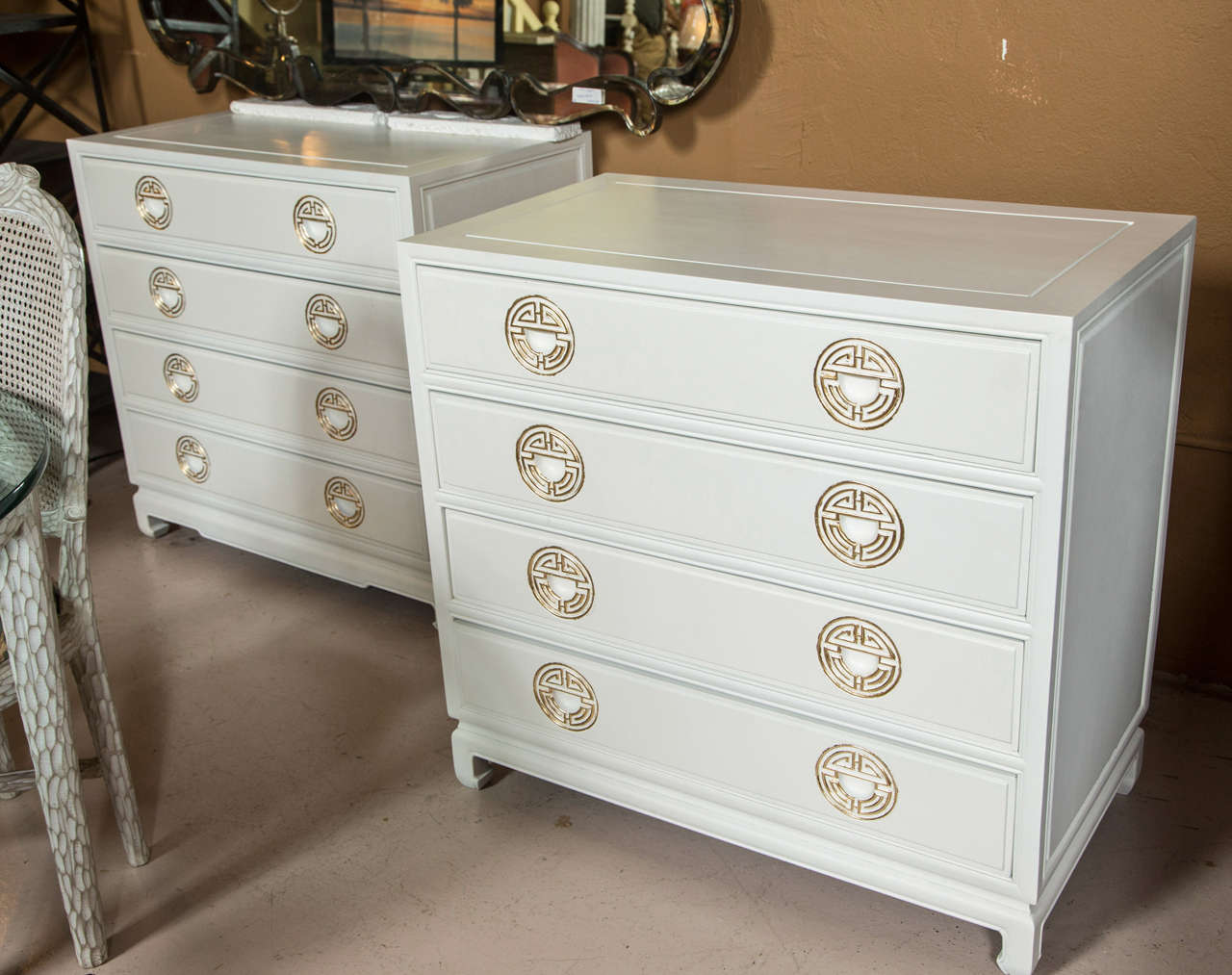 Pair of Chinese influenced bachelor chests or commodes. Part of our Winter White collection. This is a fine pair of Mid-Century Modern Chinese influenced chests. Each on bracket feet with four drawers and gilt gold pulls.