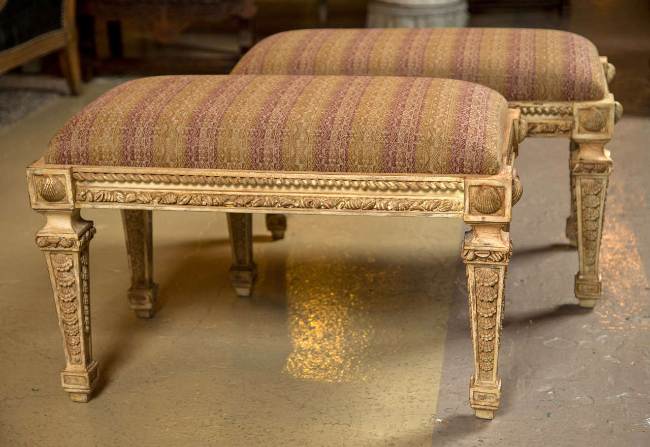 A fine pair of Louis XVI Style Benches in the Hollywood Regency taste. The tapering shell carved legs supporting a carved apron. The overall structure in a distressed and gilt finish. Recently upholstered.