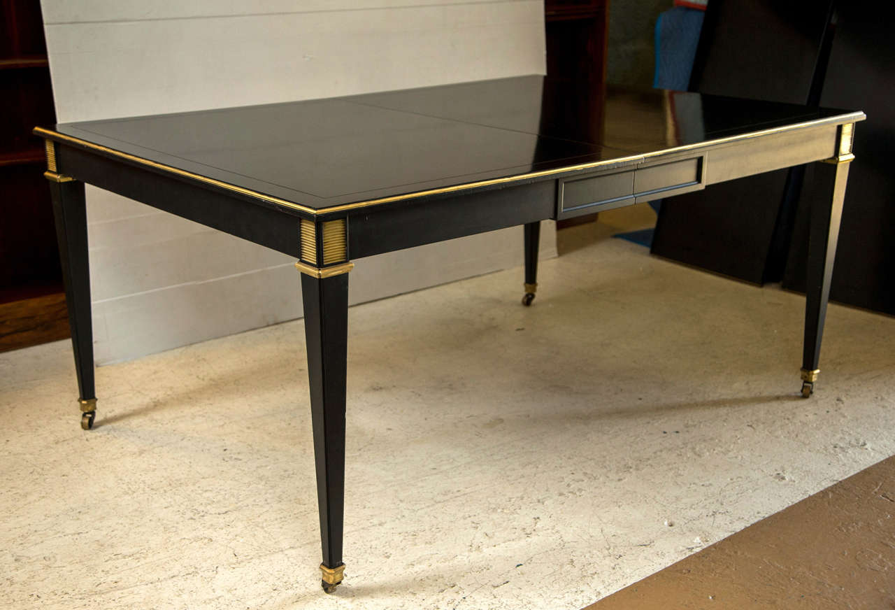This finely Ebonized Dining Table having 3 Leaves, each 19.5 inches in width. The bronze sabots leading to a square tapering leg terminating in cookie cutter corners. The top having a gilt bronze border and routered framed surface. Recently