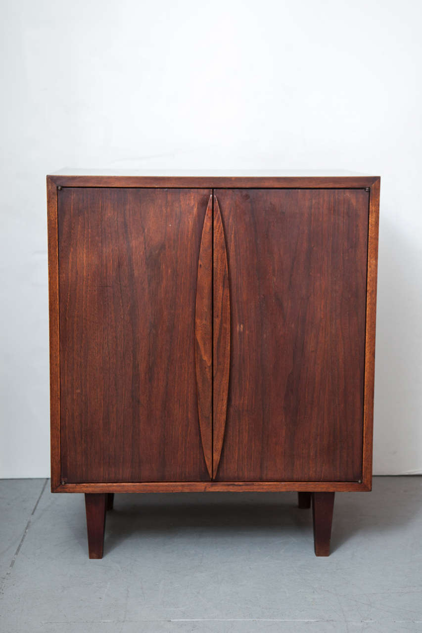 Walnut two-door dry bar / cabinet with stylized handles and resting on four legs, with two adjustable interior shelves.  Sweden, circa 1960.  

Dimensions below; height of legs/floor clearance 5.75 inches H.