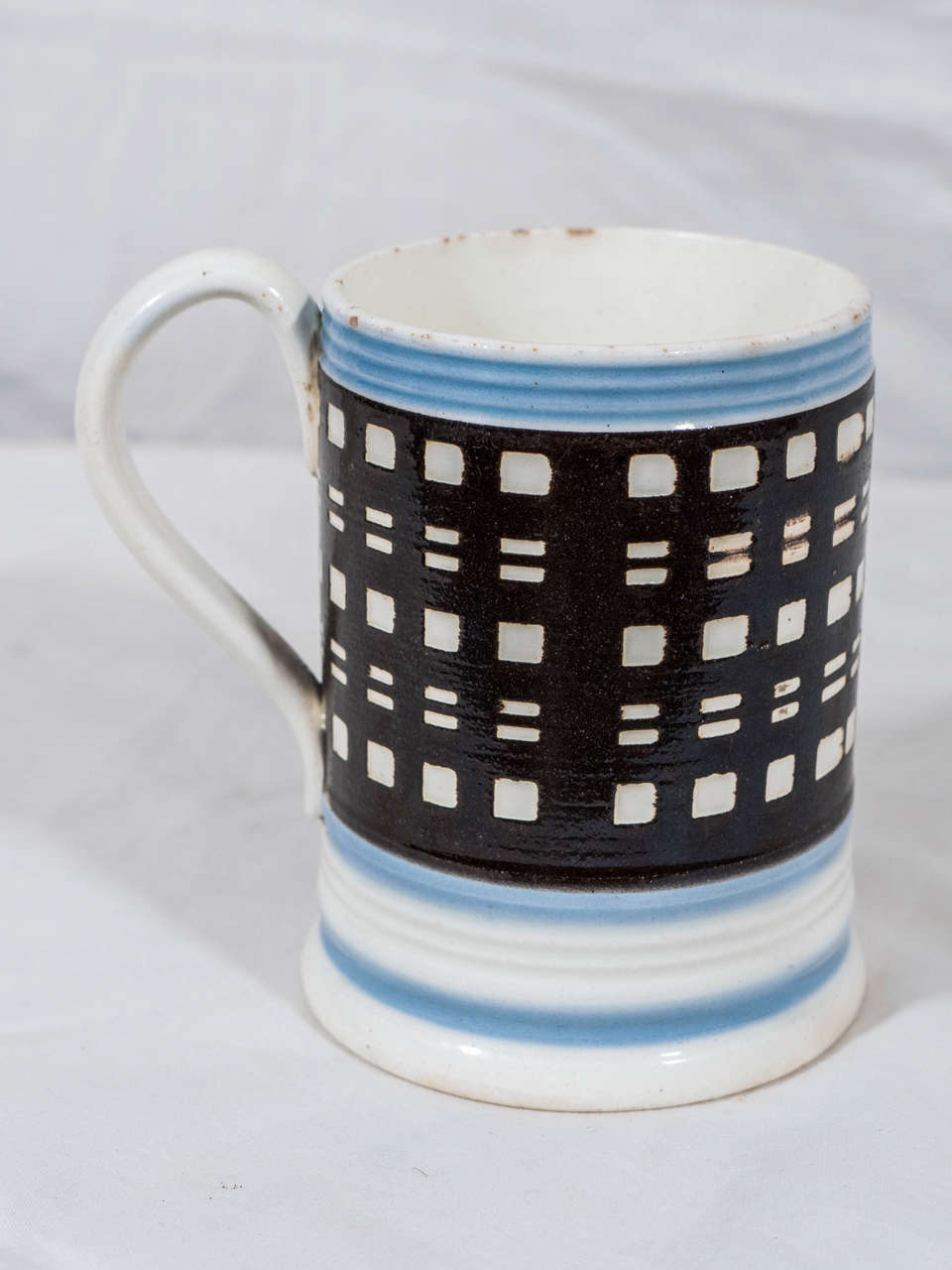 A mocha mug with a surprising, modern geometric look. It is decorated with horizontal bands of light blue above and below a large band of black slip with engine turned horizontal cuts through the black slip forming checks and rectangles.
For images